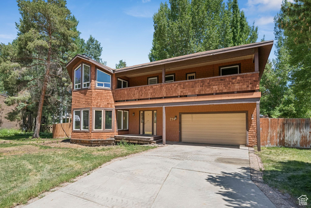 View of front facade with a balcony, a garage, concrete driveway, and a porch