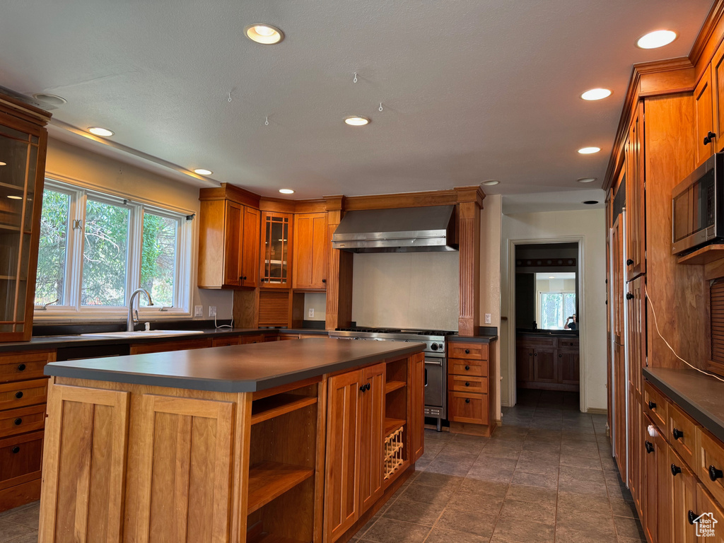 Kitchen with wall chimney range hood, dark countertops, open shelves, recessed lighting, and brown cabinets