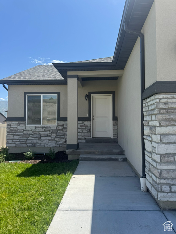 Entrance to property with stone siding, stucco siding, a lawn, and a shingled roof