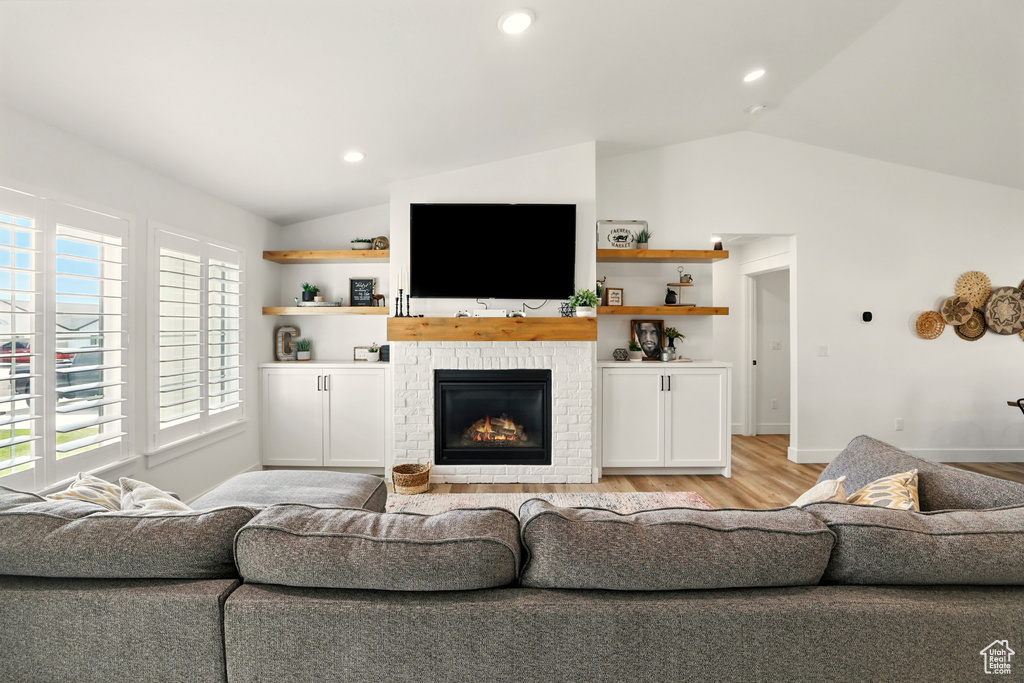 Living area with lofted ceiling, light wood-type flooring, plenty of natural light, a brick fireplace, and recessed lighting