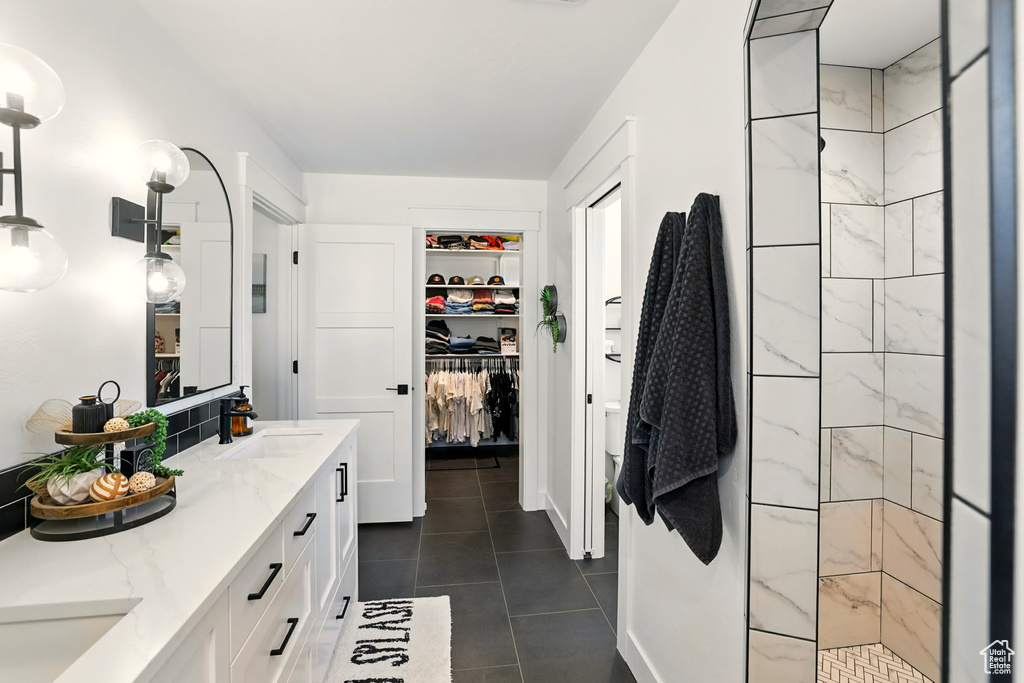 Full bath featuring double vanity, tile patterned floors, a walk in closet, and tiled shower