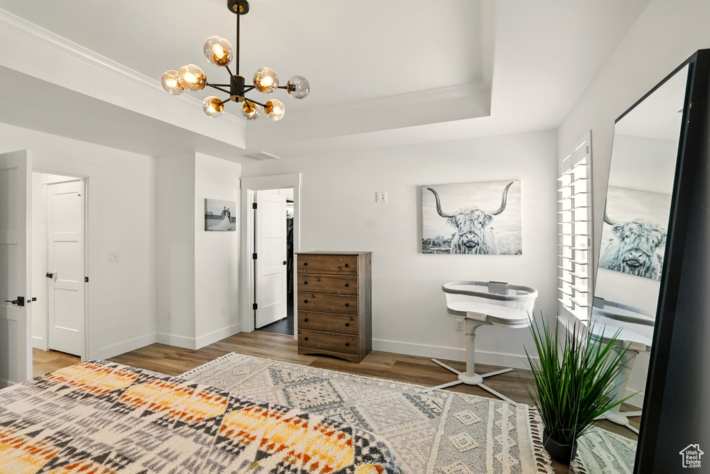 Bedroom featuring wood finished floors, a chandelier, a tray ceiling, and crown molding