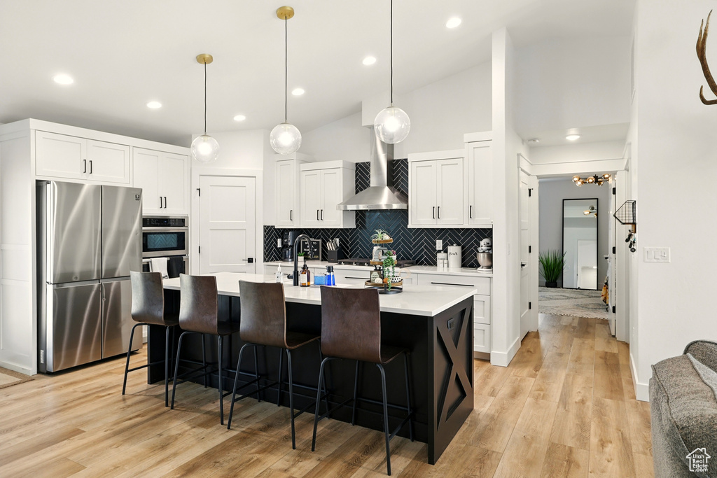 Kitchen featuring appliances with stainless steel finishes, decorative backsplash, a kitchen bar, light countertops, and white cabinets