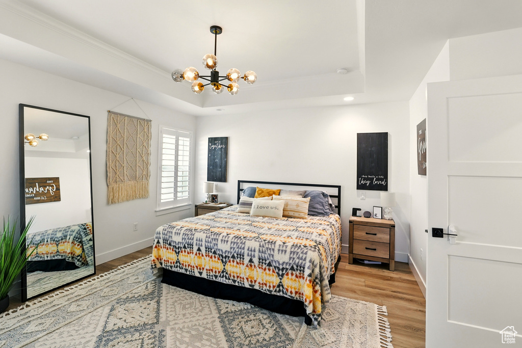Bedroom with a chandelier, light wood-style floors, a raised ceiling, recessed lighting, and crown molding