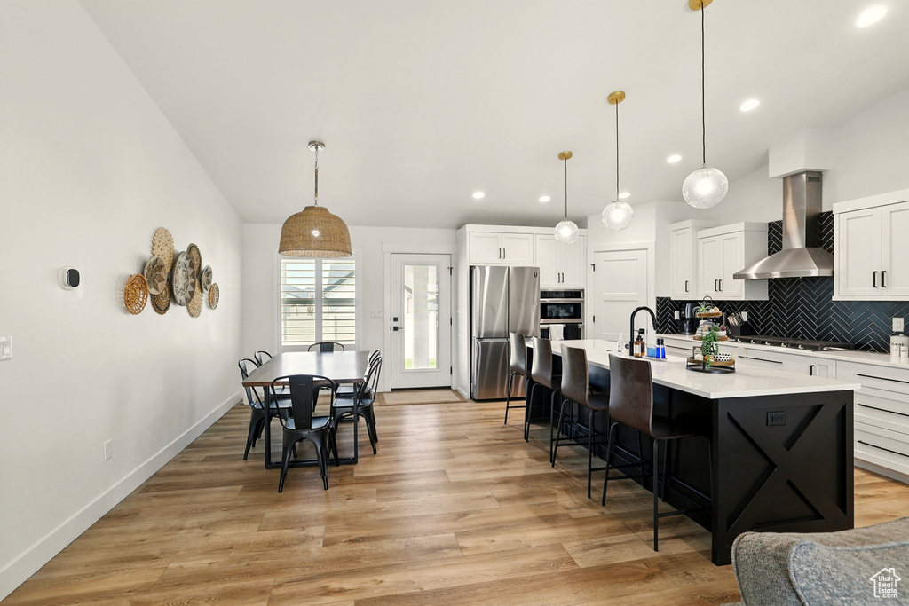 Kitchen with appliances with stainless steel finishes, wall chimney range hood, decorative backsplash, light countertops, and a kitchen breakfast bar