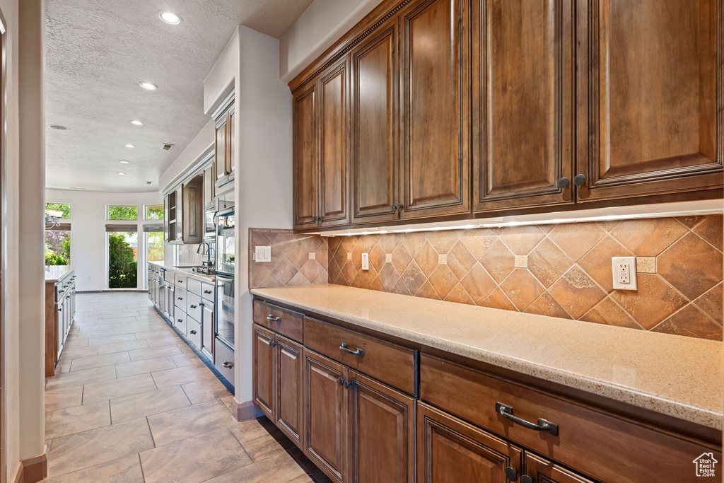 Kitchen with recessed lighting, a textured ceiling, decorative backsplash, light stone countertops, and stainless steel oven