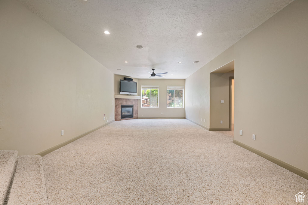 Unfurnished living room with a ceiling fan, carpet, a tiled fireplace, recessed lighting, and a textured ceiling