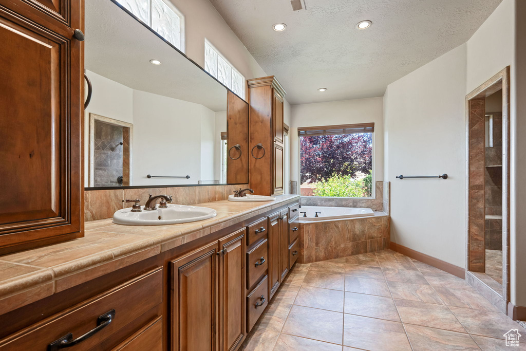 Full bathroom with a bath, double vanity, recessed lighting, a tile shower, and a textured ceiling