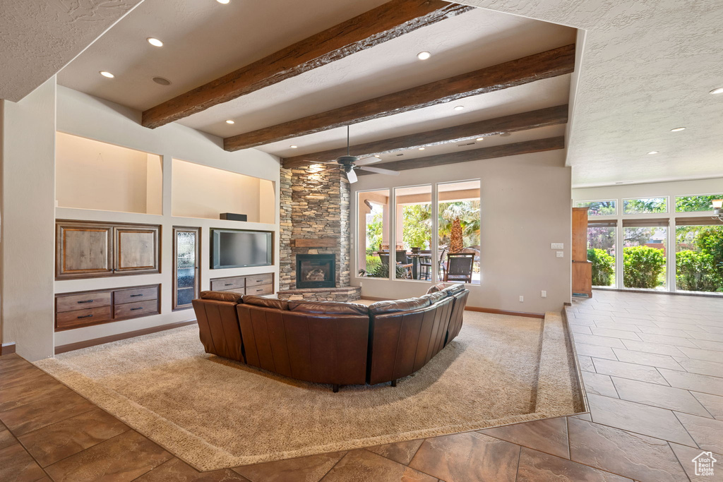 Living area featuring healthy amount of natural light, a stone fireplace, recessed lighting, a ceiling fan, and beam ceiling