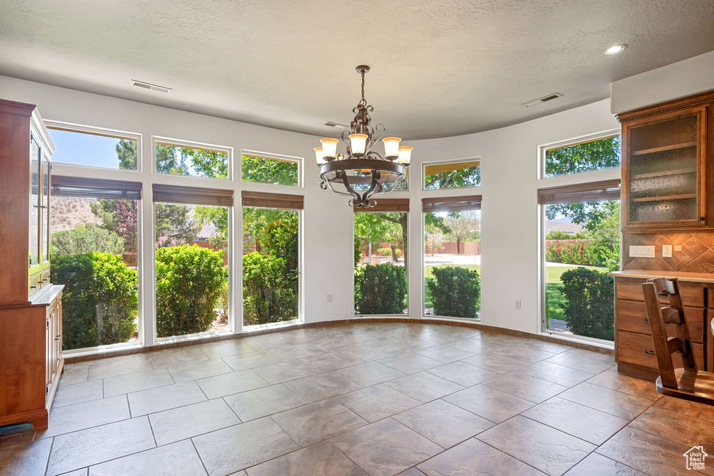 Unfurnished dining area featuring healthy amount of natural light, a chandelier, a textured ceiling, and recessed lighting