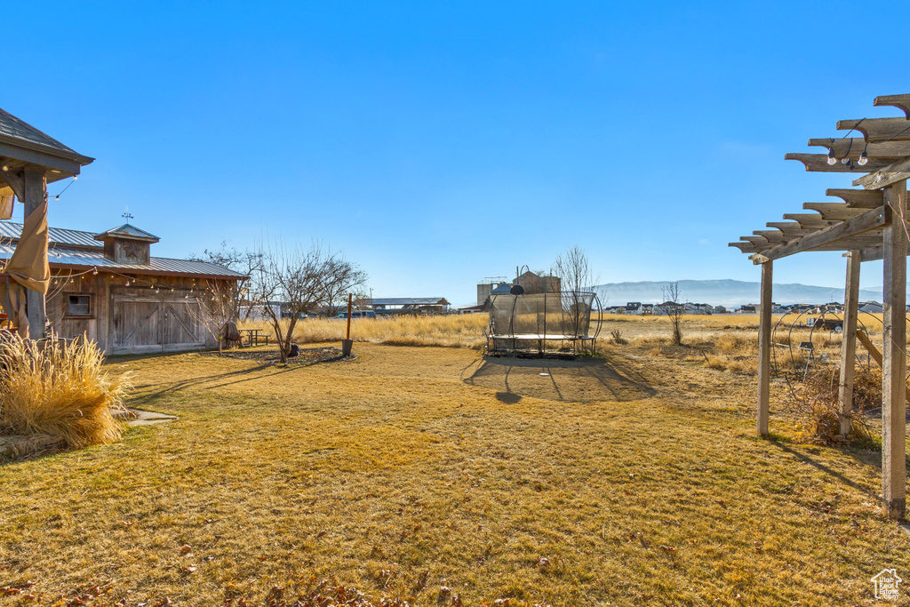 View of grassy yard featuring a trampoline, a pergola, and a mountain view