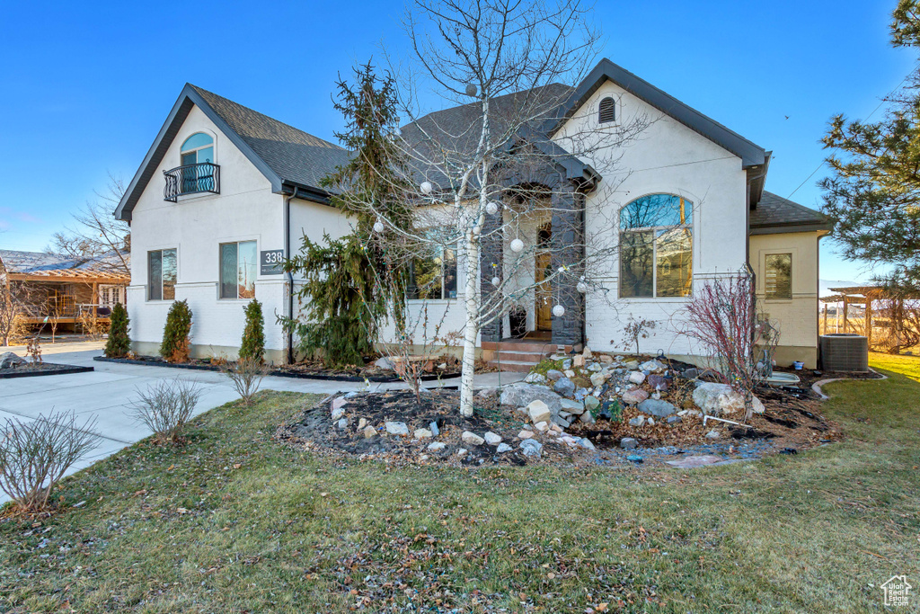 French provincial home with stucco siding, a front lawn, and roof with shingles