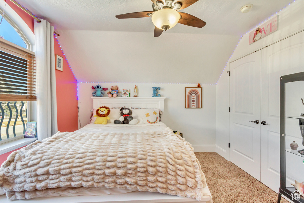 Carpeted bedroom featuring lofted ceiling, a closet, and a ceiling fan