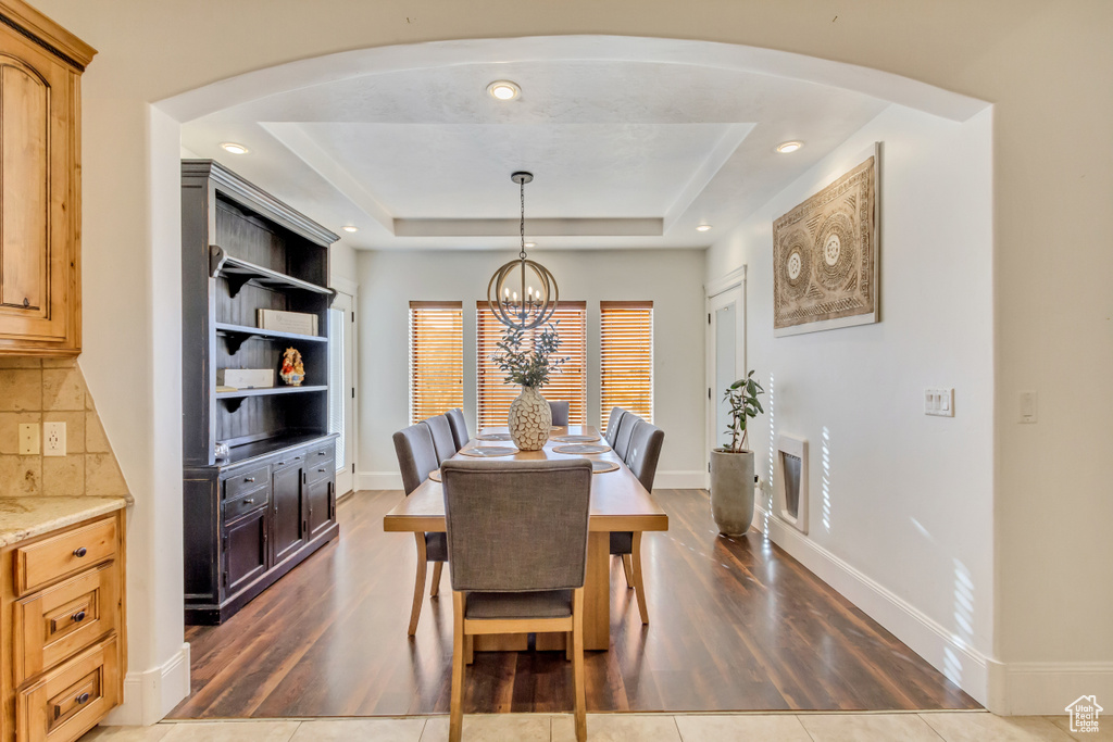Dining room featuring dark wood-style floors, a chandelier, a tray ceiling, arched walkways, and recessed lighting