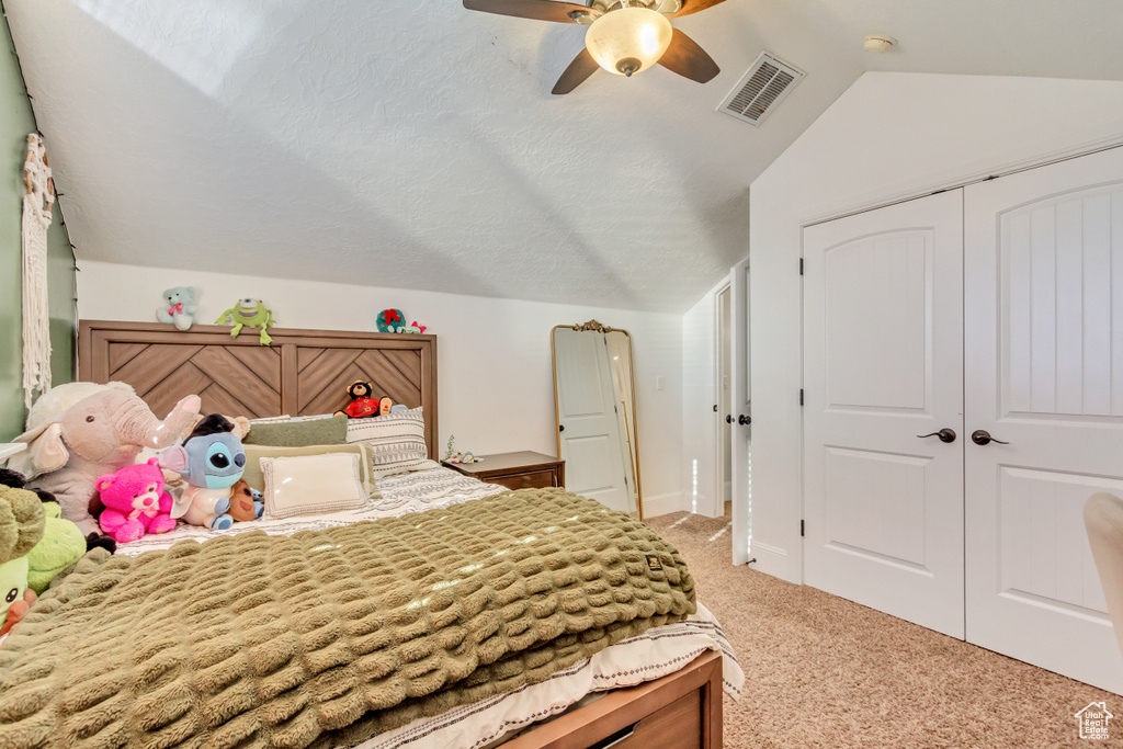 Bedroom featuring light colored carpet, vaulted ceiling, a closet, and ceiling fan
