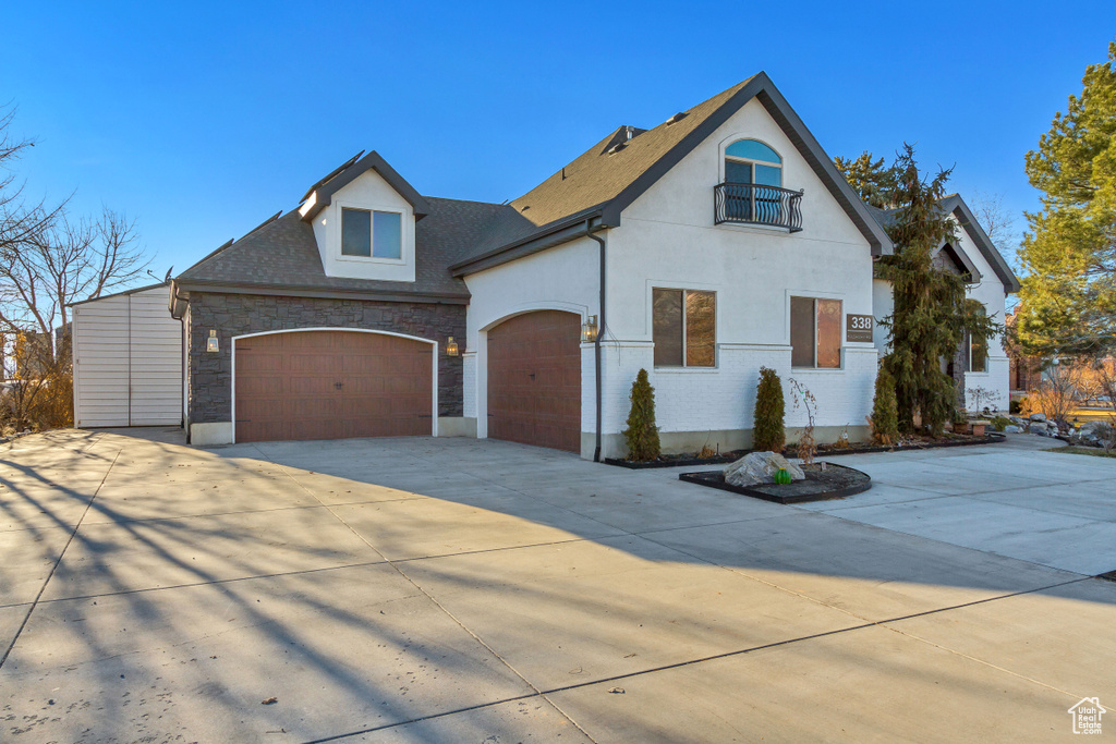 French country home with a balcony, concrete driveway, stone siding, a garage, and stucco siding
