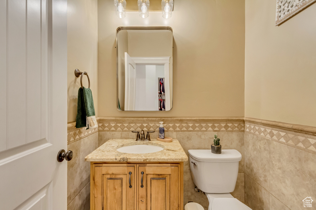 Half bathroom featuring tile walls, a wainscoted wall, and vanity