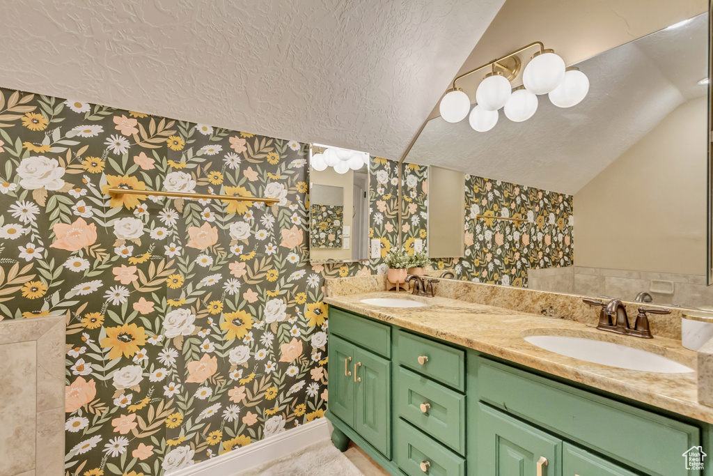 Bathroom featuring wallpapered walls, lofted ceiling, a textured ceiling, and double vanity