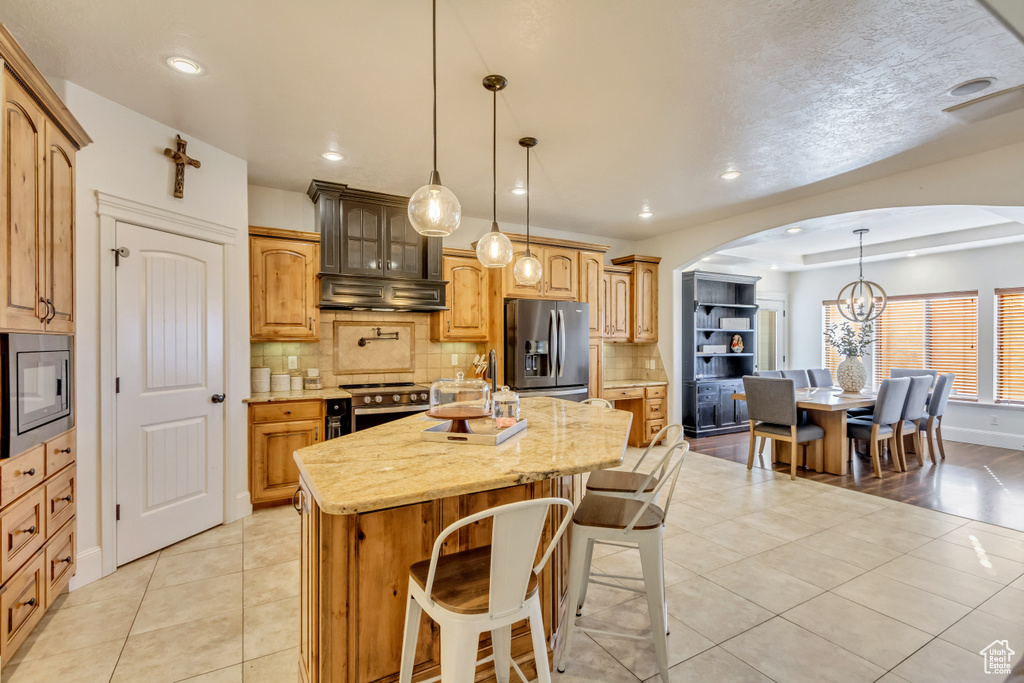 Kitchen with stainless steel appliances, arched walkways, a kitchen island, tasteful backsplash, and light tile patterned floors