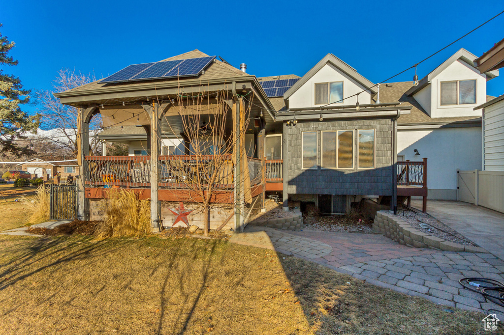 Back of house with solar panels, a shingled roof, stucco siding, and a gate