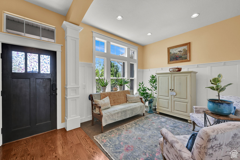 Living room featuring a decorative wall, ornate columns, a wainscoted wall, wood finished floors, and recessed lighting