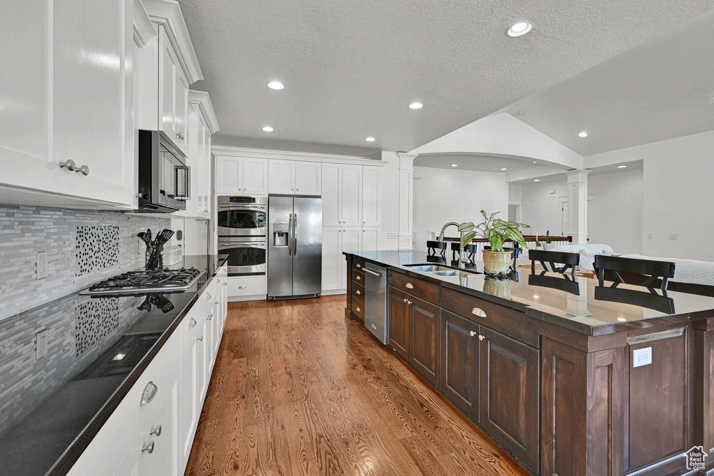 Kitchen with decorative columns, appliances with stainless steel finishes, wood finished floors, white cabinetry, and dark brown cabinetry