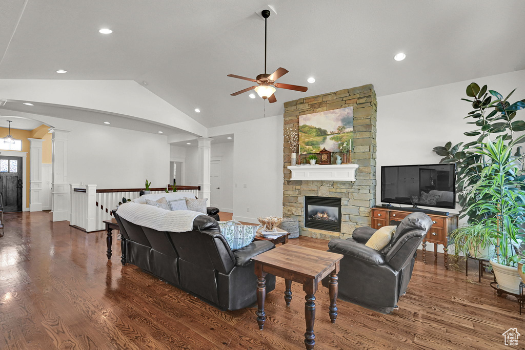 Living area with ornate columns, a ceiling fan, wood finished floors, vaulted ceiling, and a stone fireplace