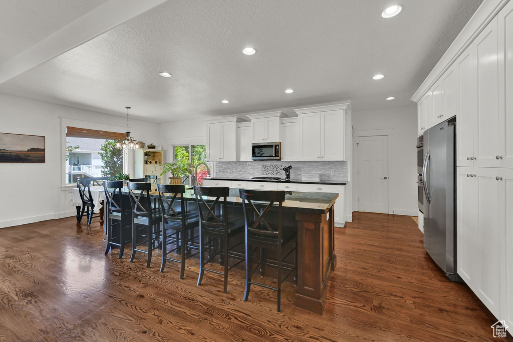 Kitchen featuring appliances with stainless steel finishes, dark wood-style floors, white cabinets, a center island with sink, and recessed lighting