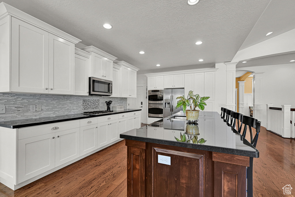 Kitchen featuring decorative columns, stainless steel appliances, dark countertops, dark wood finished floors, and recessed lighting