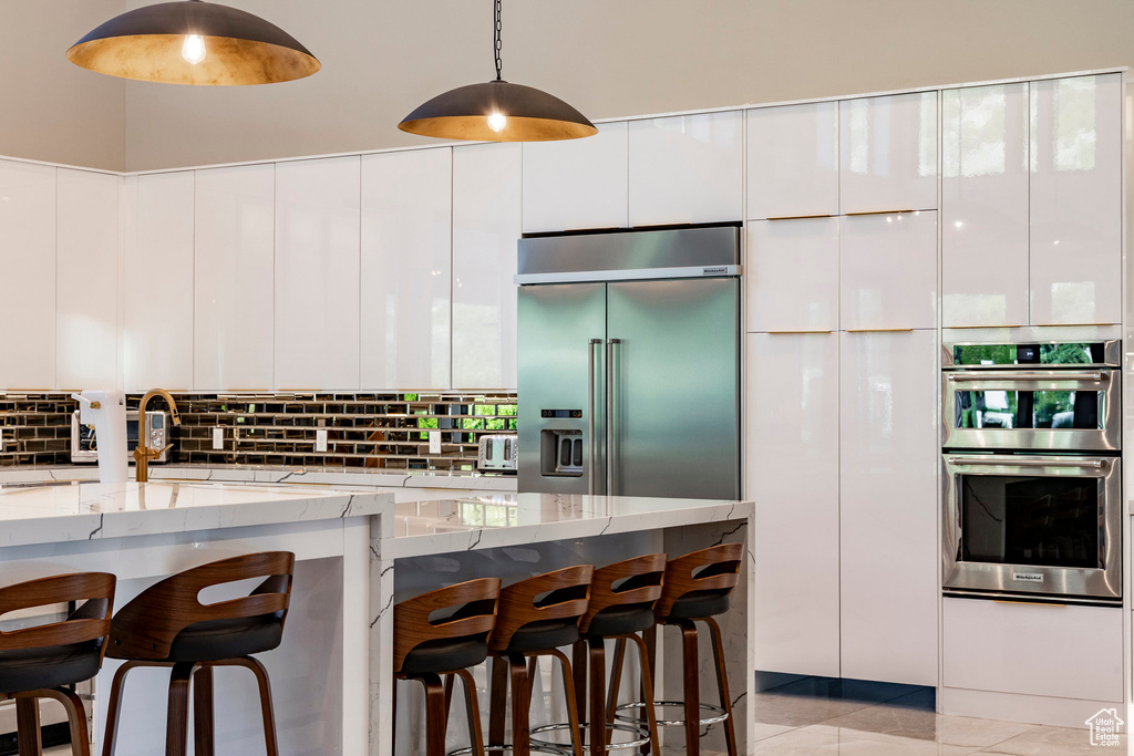 Kitchen featuring appliances with stainless steel finishes, modern cabinets, light stone counters, and a kitchen bar