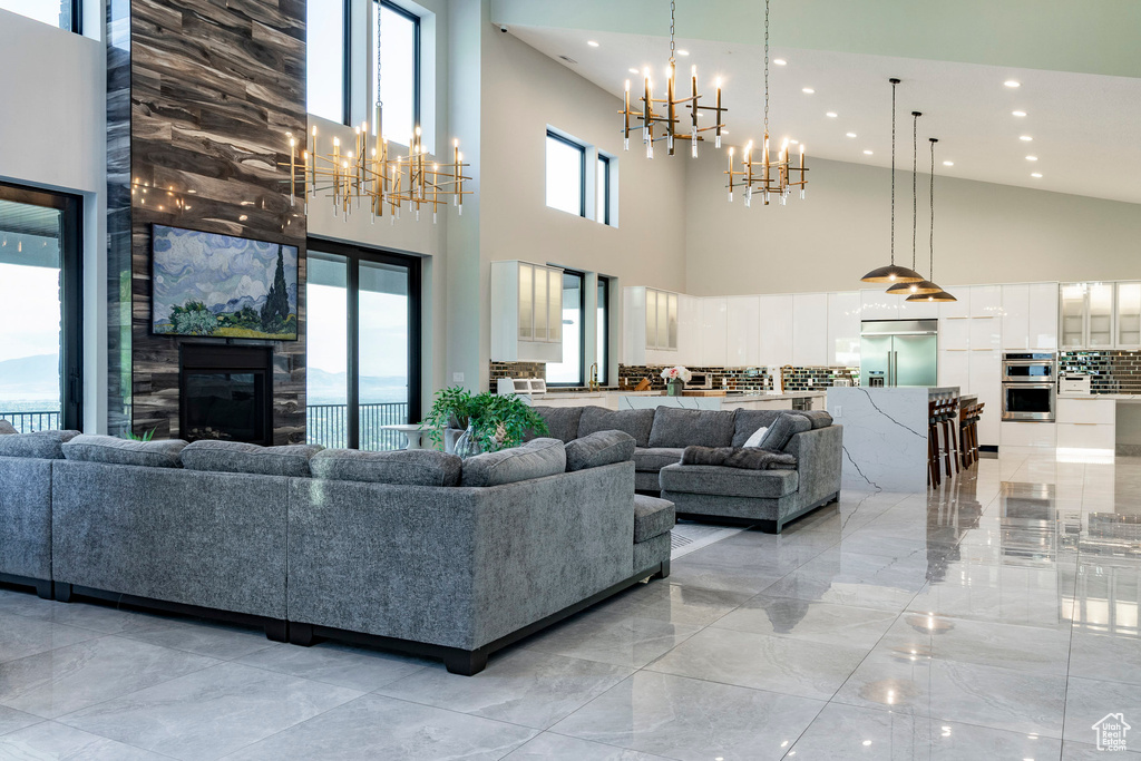 Living room with a chandelier, recessed lighting, light marble finish floors, high vaulted ceiling, and a fireplace