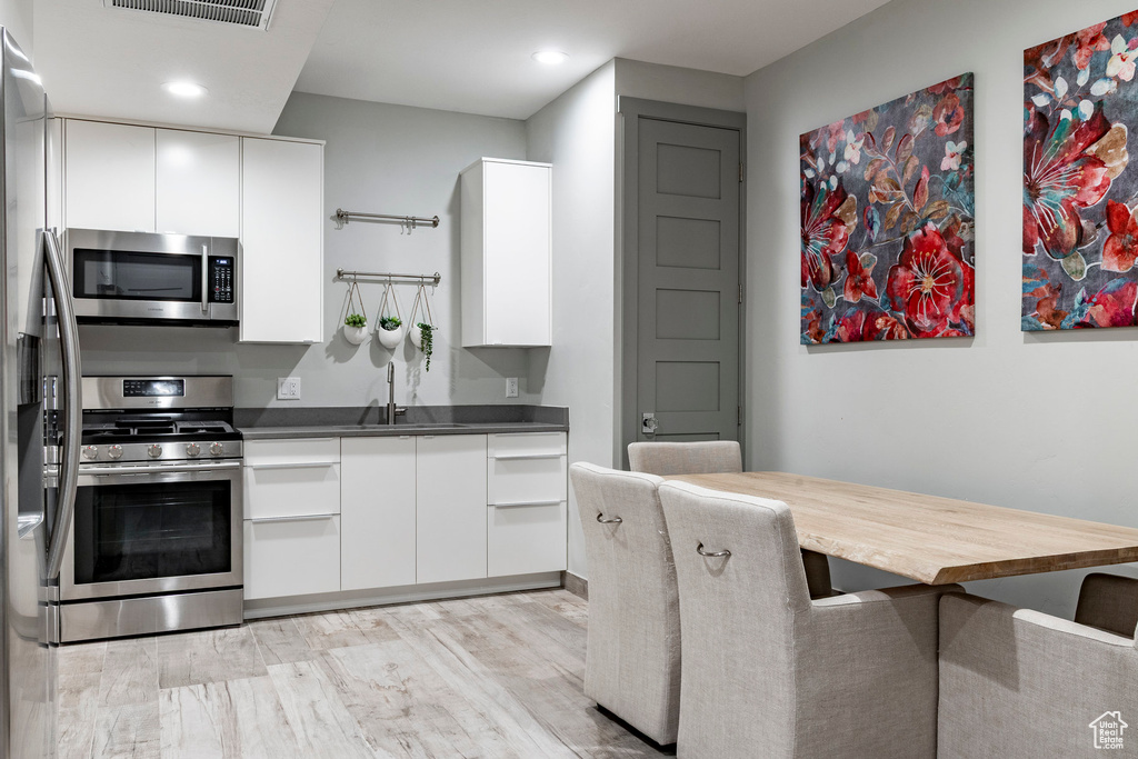 Kitchen featuring appliances with stainless steel finishes, white cabinets, recessed lighting, light wood finished floors, and modern cabinets