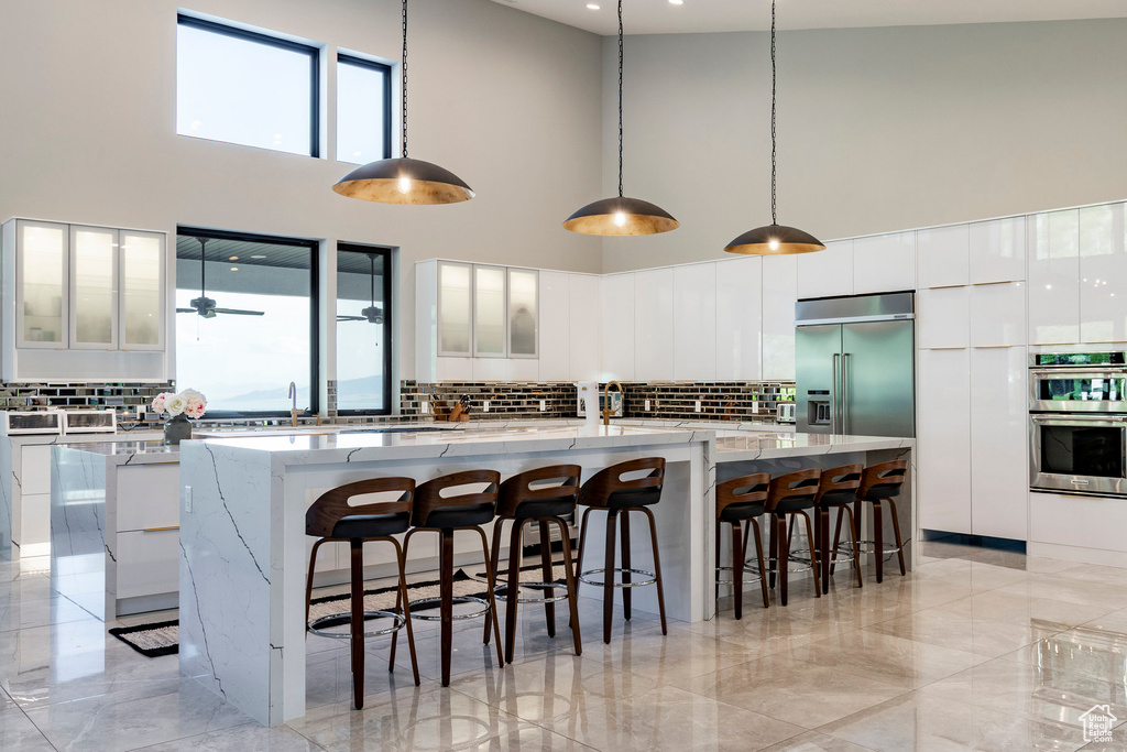Kitchen featuring a high ceiling, appliances with stainless steel finishes, decorative backsplash, white cabinets, and a spacious island