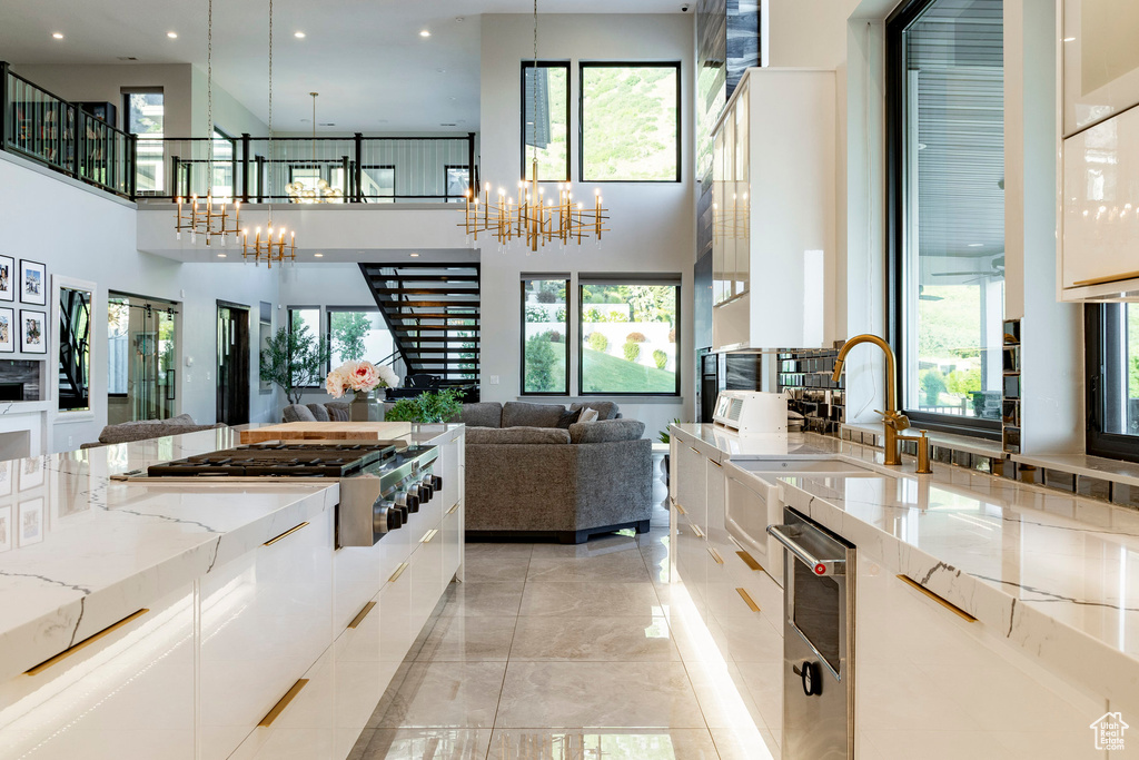 Kitchen with a chandelier, modern cabinets, a towering ceiling, white cabinetry, and recessed lighting