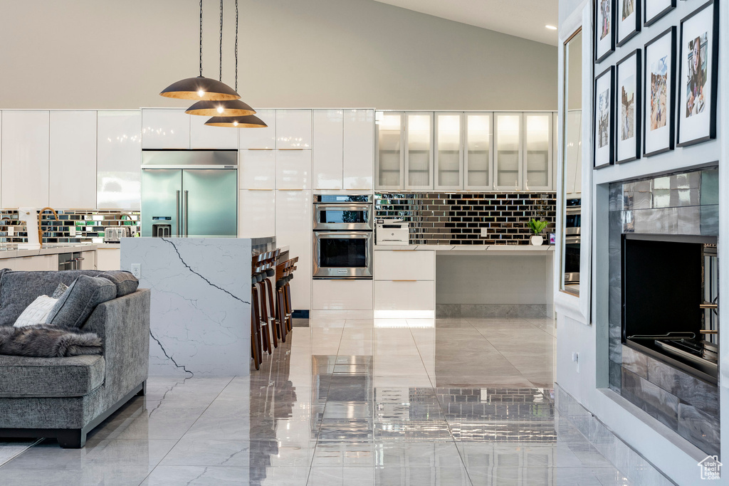 Kitchen with modern cabinets, appliances with stainless steel finishes, high vaulted ceiling, tasteful backsplash, and white cabinets