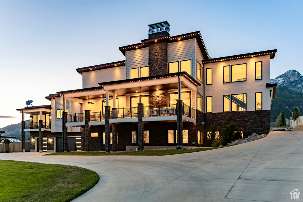 Back of house with stone siding, a balcony, curved driveway, a chimney, and stucco siding