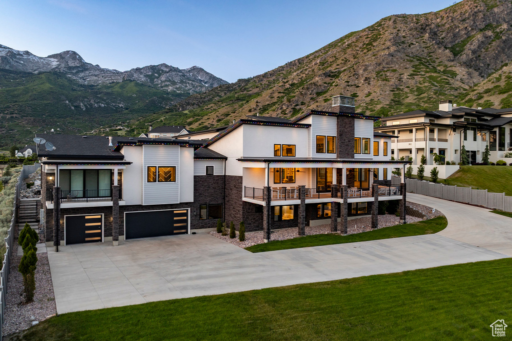 View of front of property featuring stone siding, a balcony, concrete driveway, an attached garage, and a mountain view