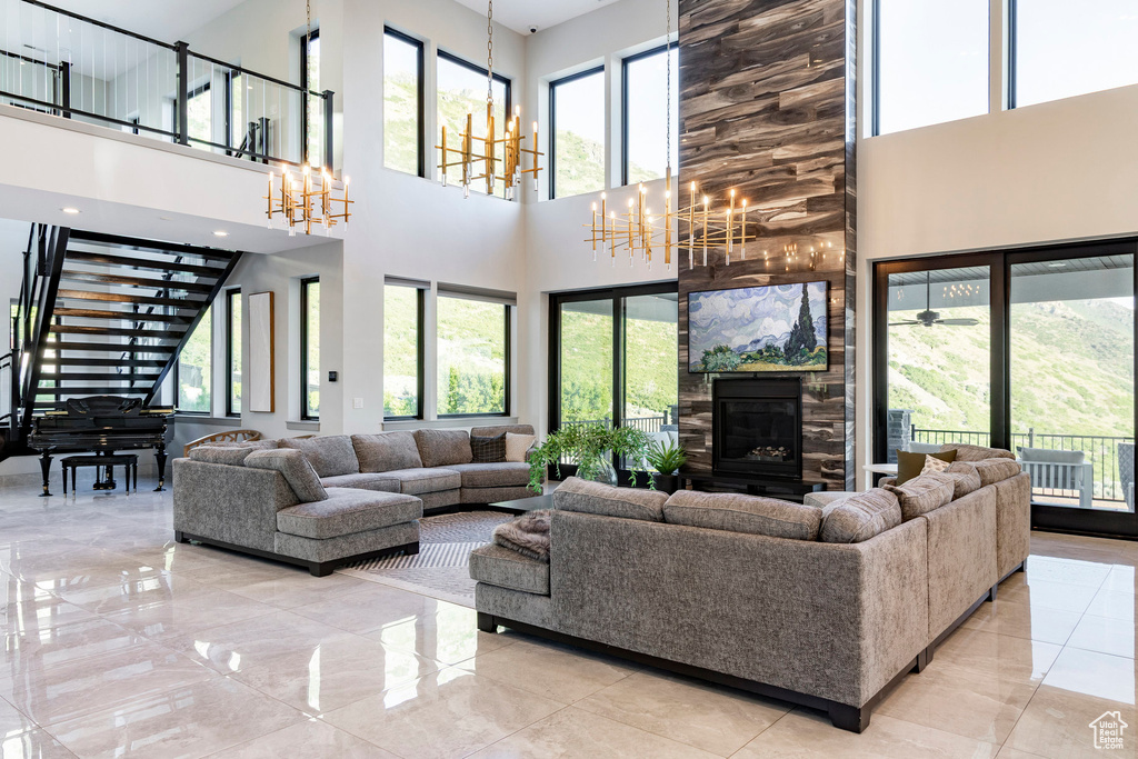 Living area featuring a chandelier, a towering ceiling, a stone fireplace, stairway, and marble tiled floors