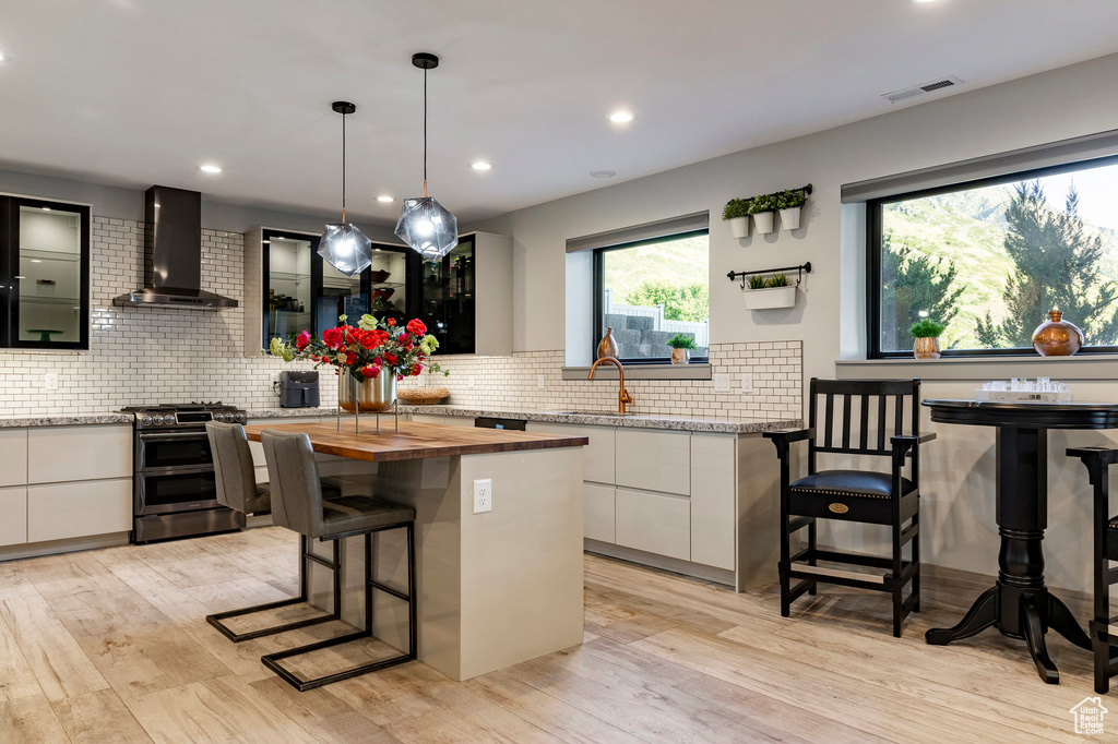 Kitchen featuring range with two ovens, wall chimney range hood, a kitchen bar, modern cabinets, and white cabinets