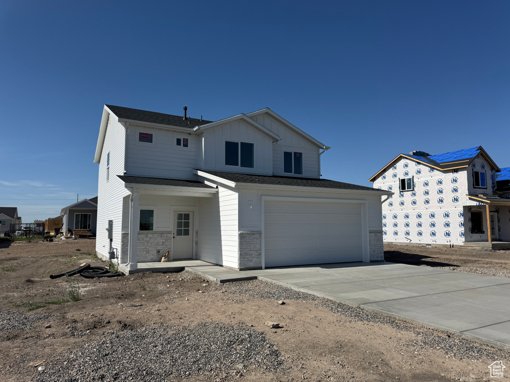 View of front facade with concrete driveway, an attached garage, board and batten siding, and stone siding