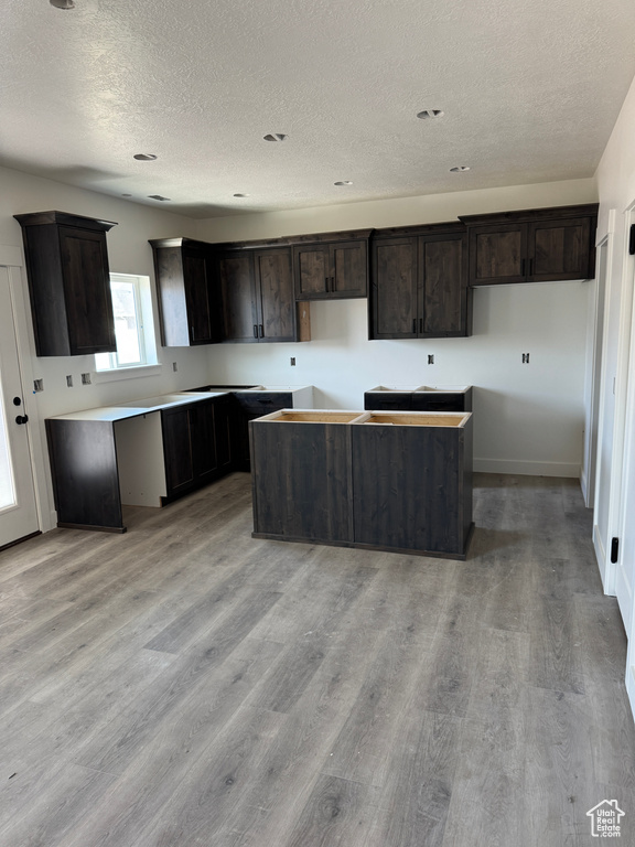 Kitchen with a textured ceiling, a kitchen island, light wood finished floors, and dark brown cabinets