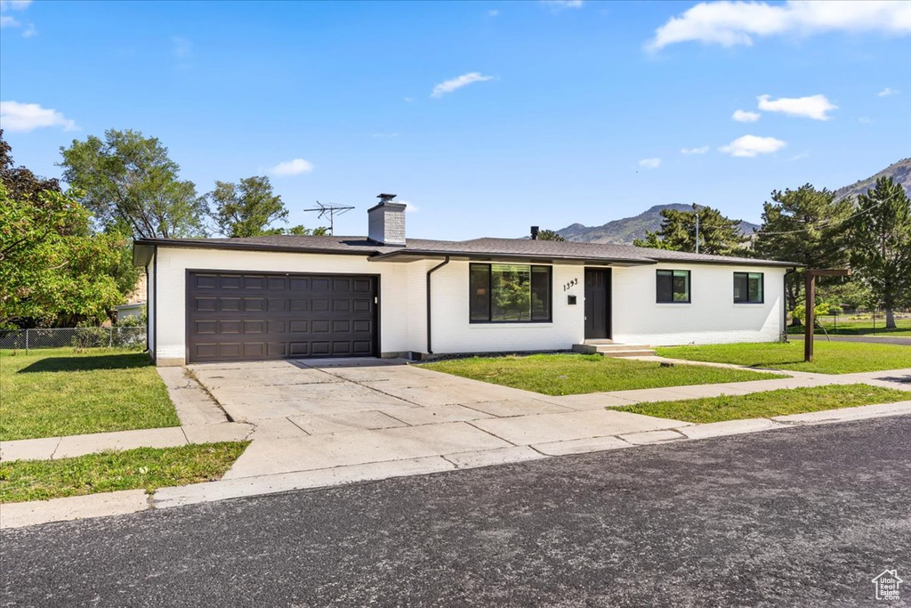 Ranch-style home featuring a garage, a front lawn, a chimney, and driveway