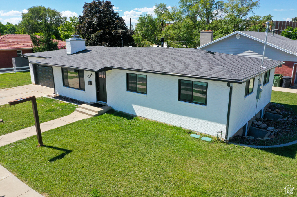 View of front of house featuring a chimney, a shingled roof, an attached garage, and a front lawn