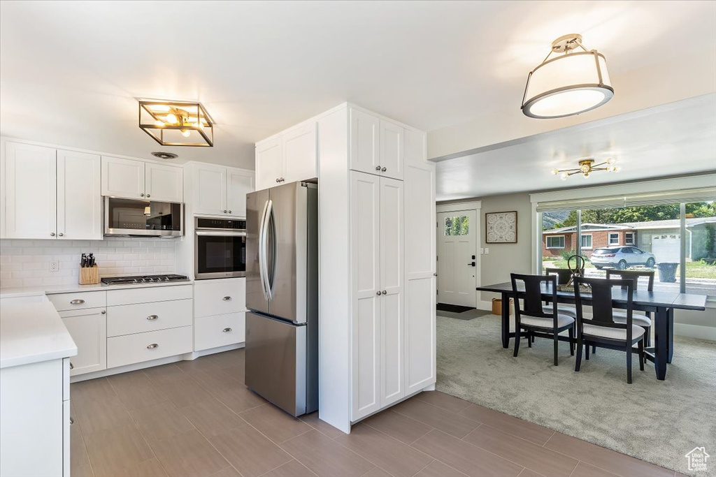 Kitchen featuring appliances with stainless steel finishes, light countertops, decorative backsplash, white cabinets, and light wood finished floors