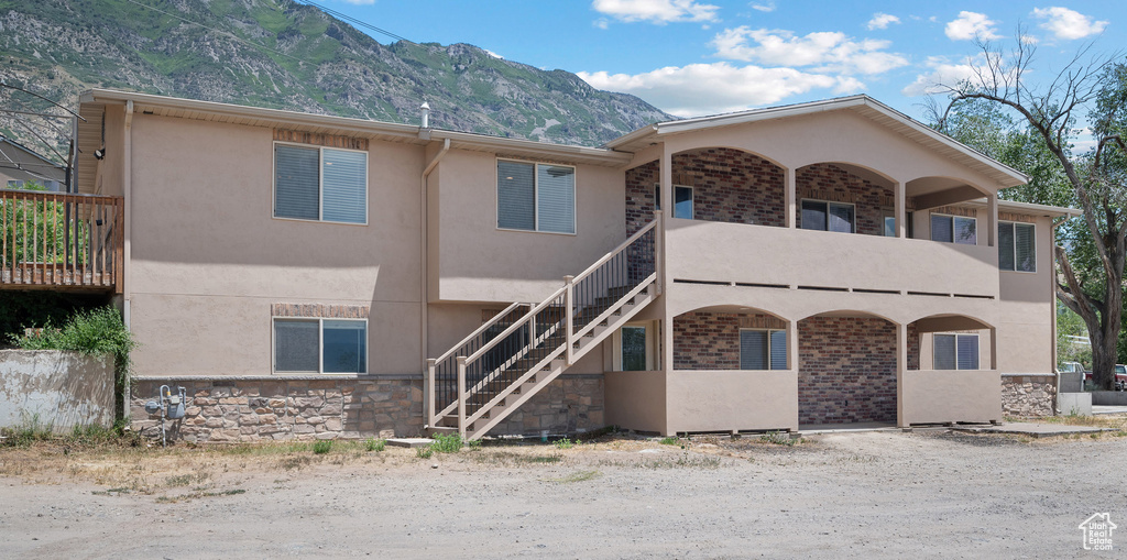 View of front facade featuring stucco siding, a mountain view, stairway, stone siding, and a balcony