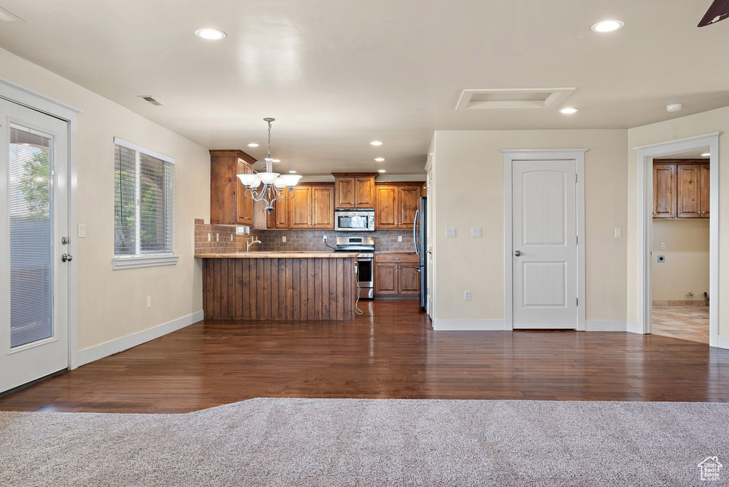 Kitchen featuring appliances with stainless steel finishes, brown cabinetry, a peninsula, dark wood finished floors, and recessed lighting