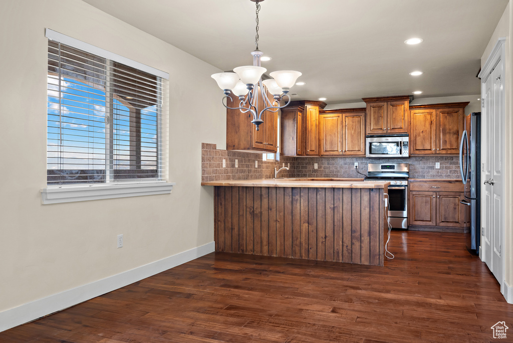 Kitchen featuring stainless steel appliances, brown cabinetry, a chandelier, a peninsula, and backsplash