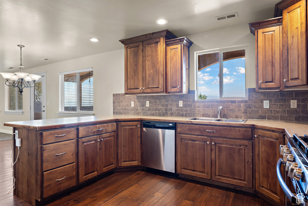 Kitchen featuring appliances with stainless steel finishes, a peninsula, a chandelier, dark wood-style flooring, and light countertops