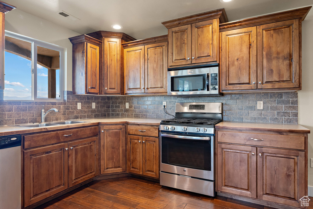 Kitchen with stainless steel appliances, light countertops, dark wood-type flooring, backsplash, and recessed lighting