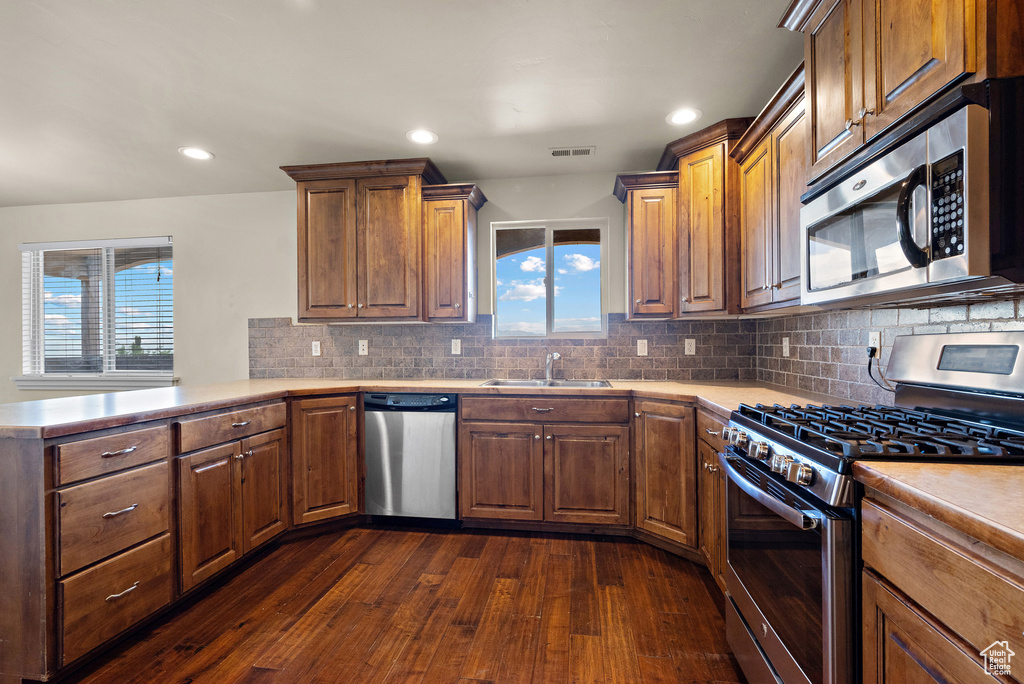 Kitchen with stainless steel appliances, dark wood-style flooring, light countertops, tasteful backsplash, and recessed lighting